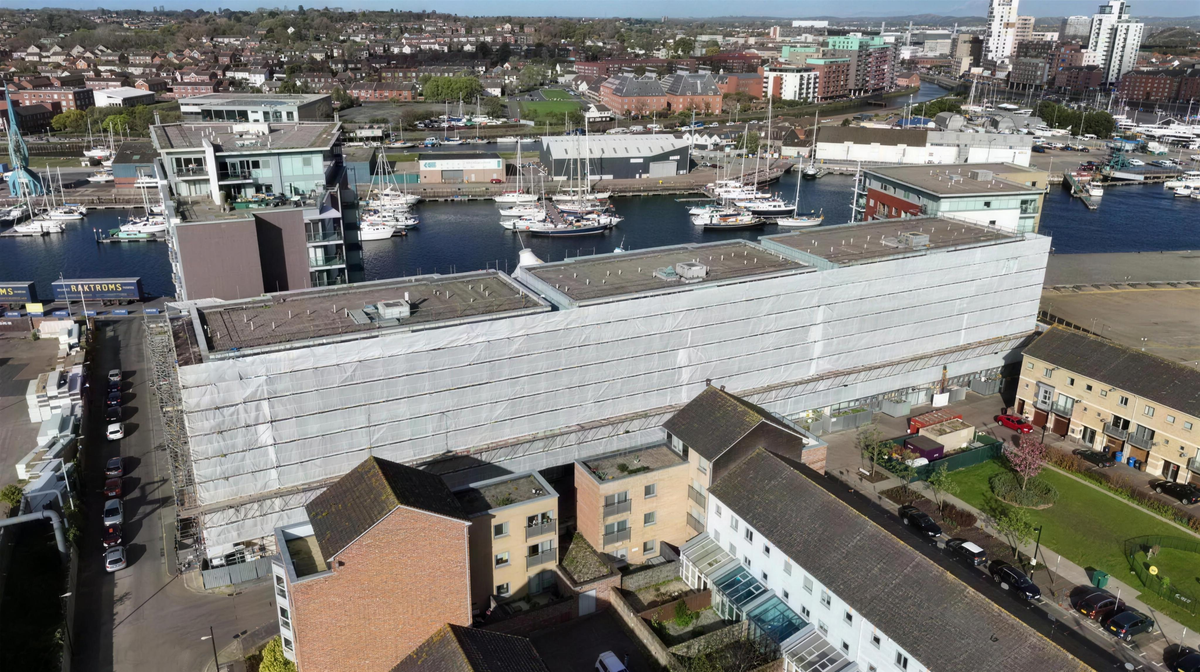 Full building wrap beside a working marina, filmed from the air